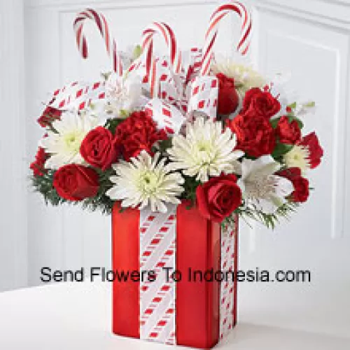 Ce bouquet les éblouira par sa joie fantaisiste et sa beauté pleine d'énergie ! Un magnifique arrangement de chrysanthèmes blancs, de œillets rouges et de roses spray est niché parmi des verdure de Noël dans un vase rouge brillant orné de cannes de Noël et emballé à la perfection avec un joli nœud, ce qui en fait ressemble au plus beau cadeau de vacances. (Veuillez noter que nous nous réservons le droit de substituer tout produit par un produit approprié de valeur égale en cas de non-disponibilité d'un certain produit)